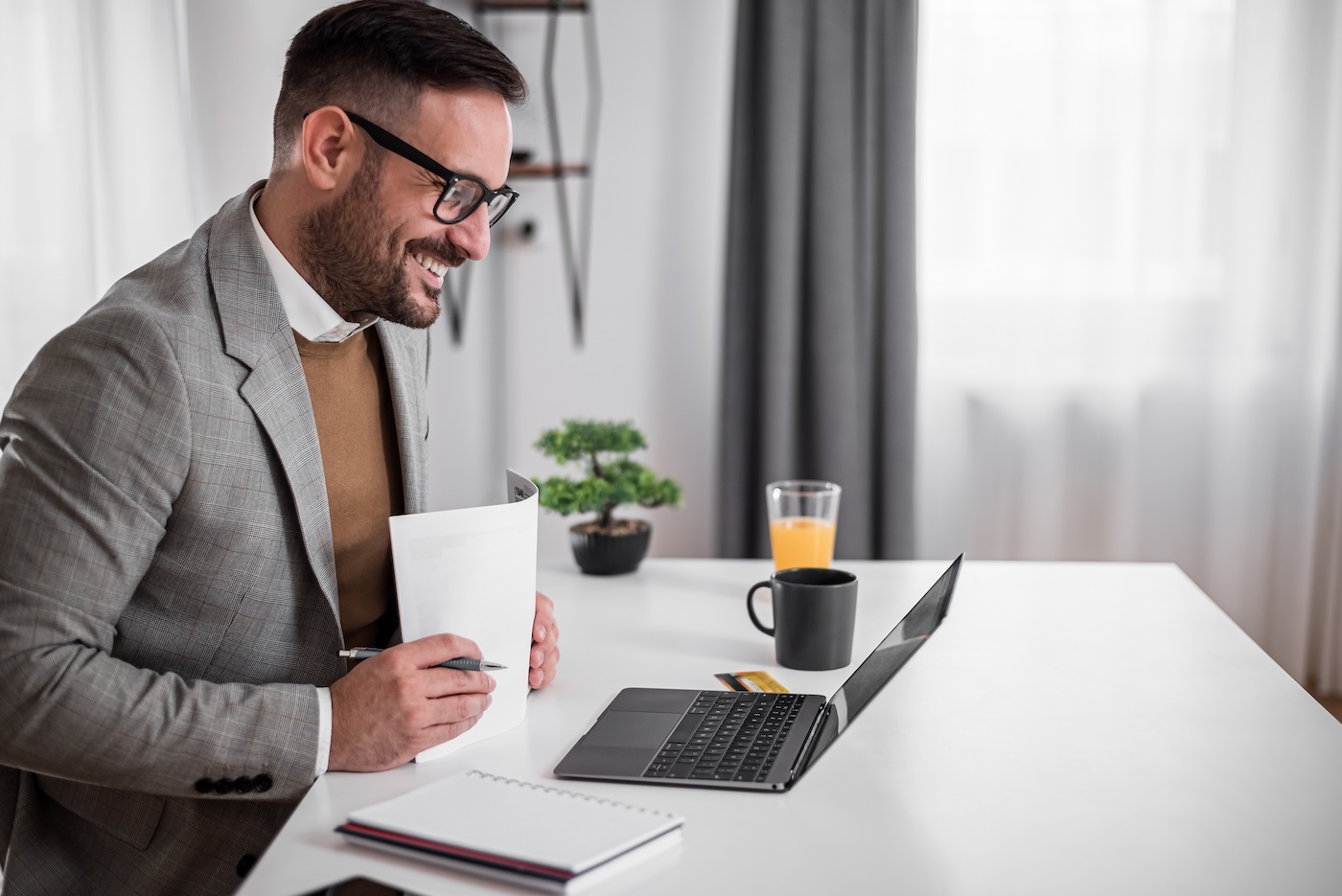 Cheerful adult bearded man, folding the files, attending an online conference call with colleagues.