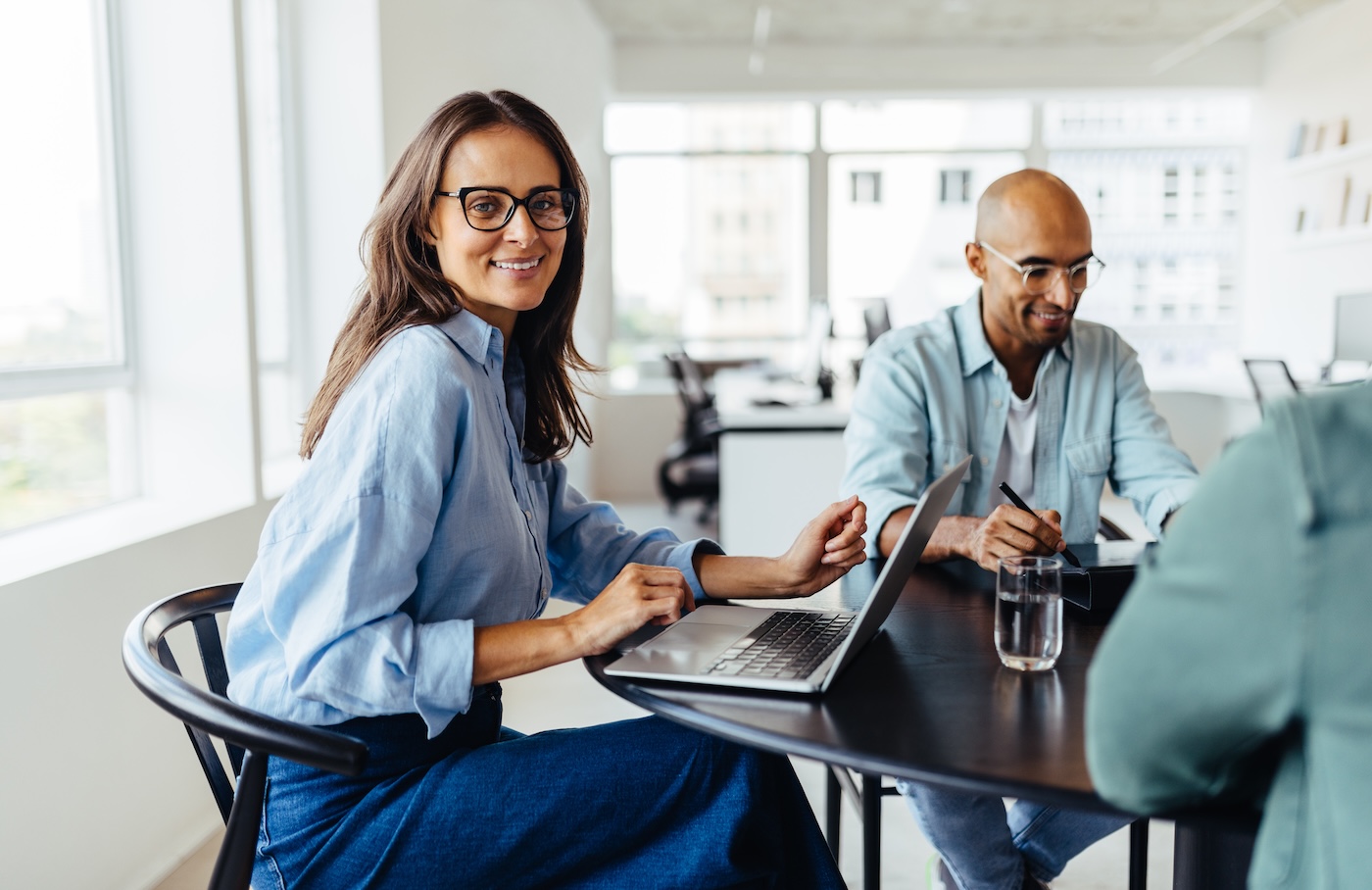 Mature female designer sitting around a table and smiling at the camera. Happy business woman having a meeting with her team in an office.