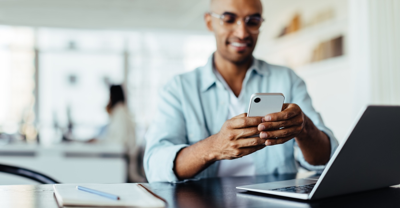 Black business man sitting in an office and using a smartphone. Happy young man working in digital marketing.